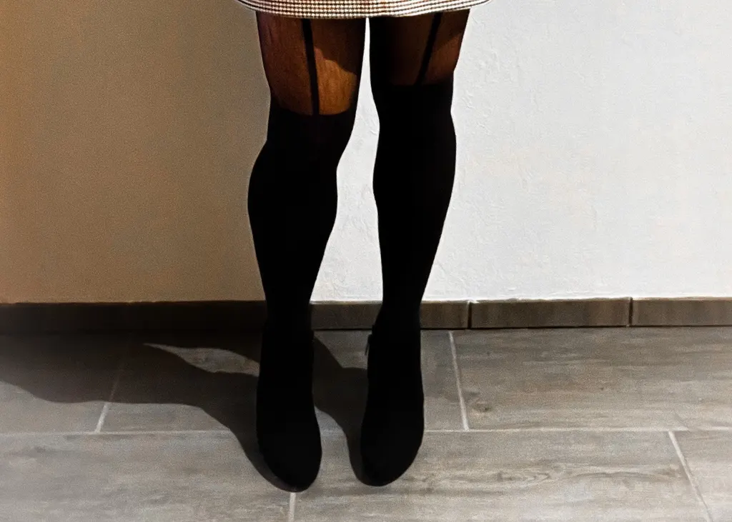 Legs in sheer tights with a suspender look and black ankle boots