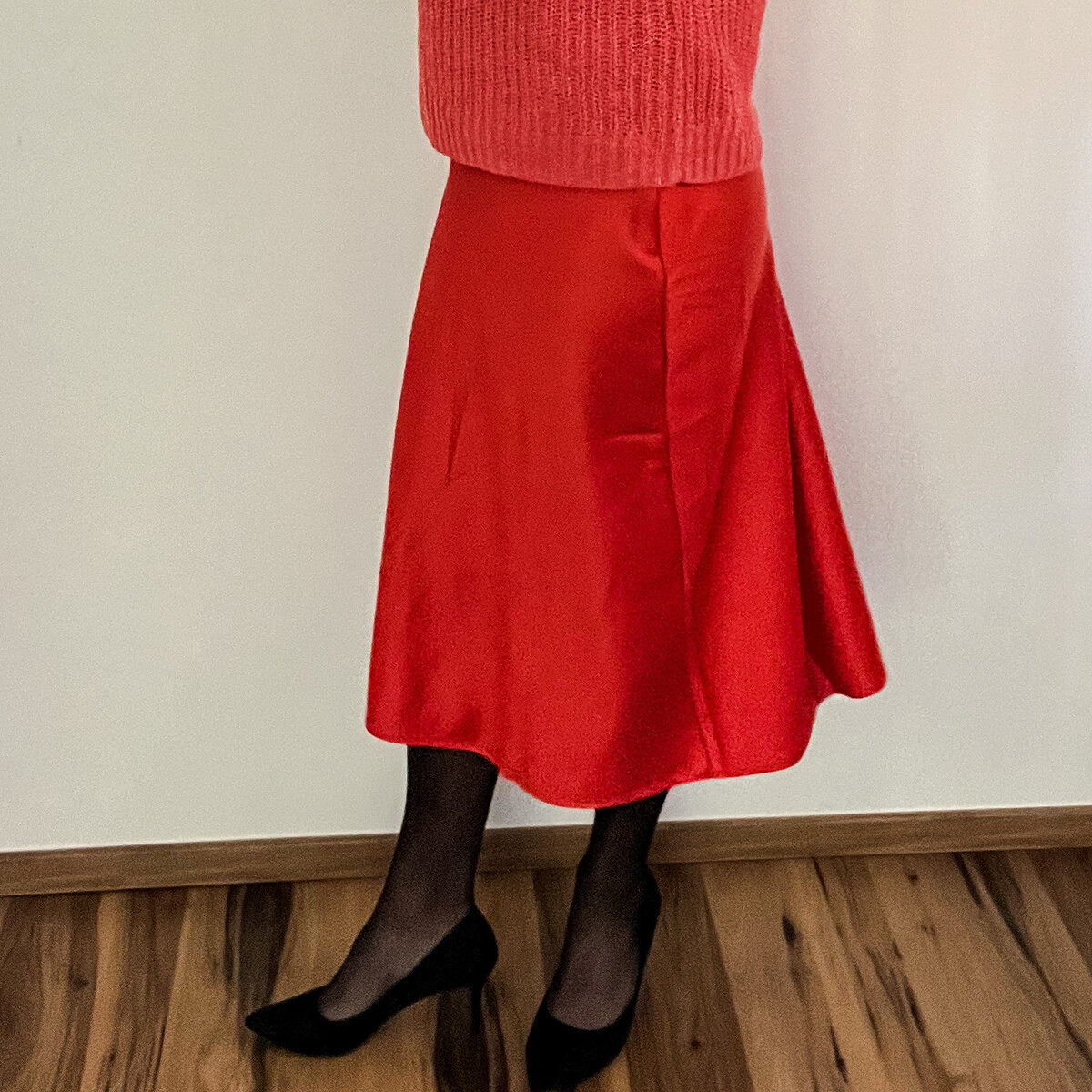 Side view: black pumps with a slim heel worn with a red satin skirt and black tights