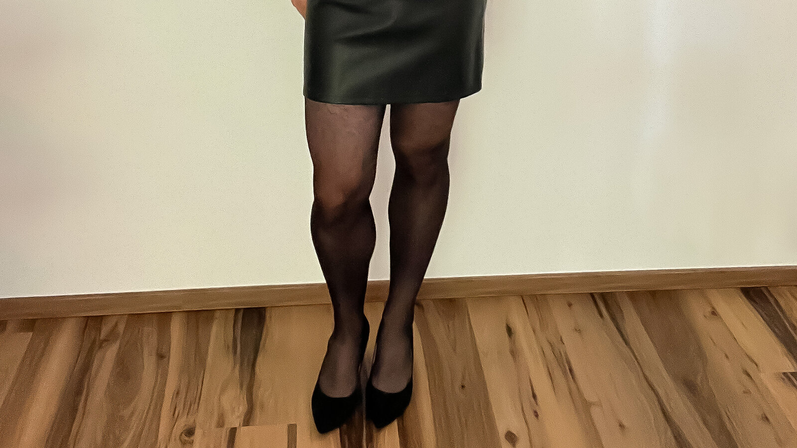 Legs in black tights with black pumps under a black leather skirt