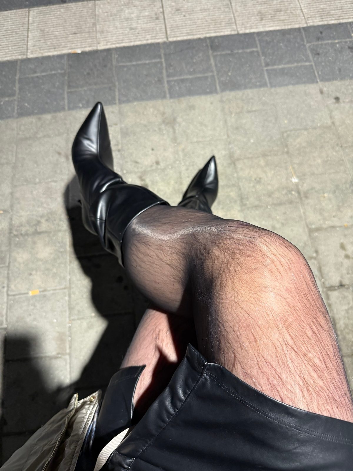 Black boots with a high heel, fine black tights and a leather skirt on the ribbed tiles of a station platform