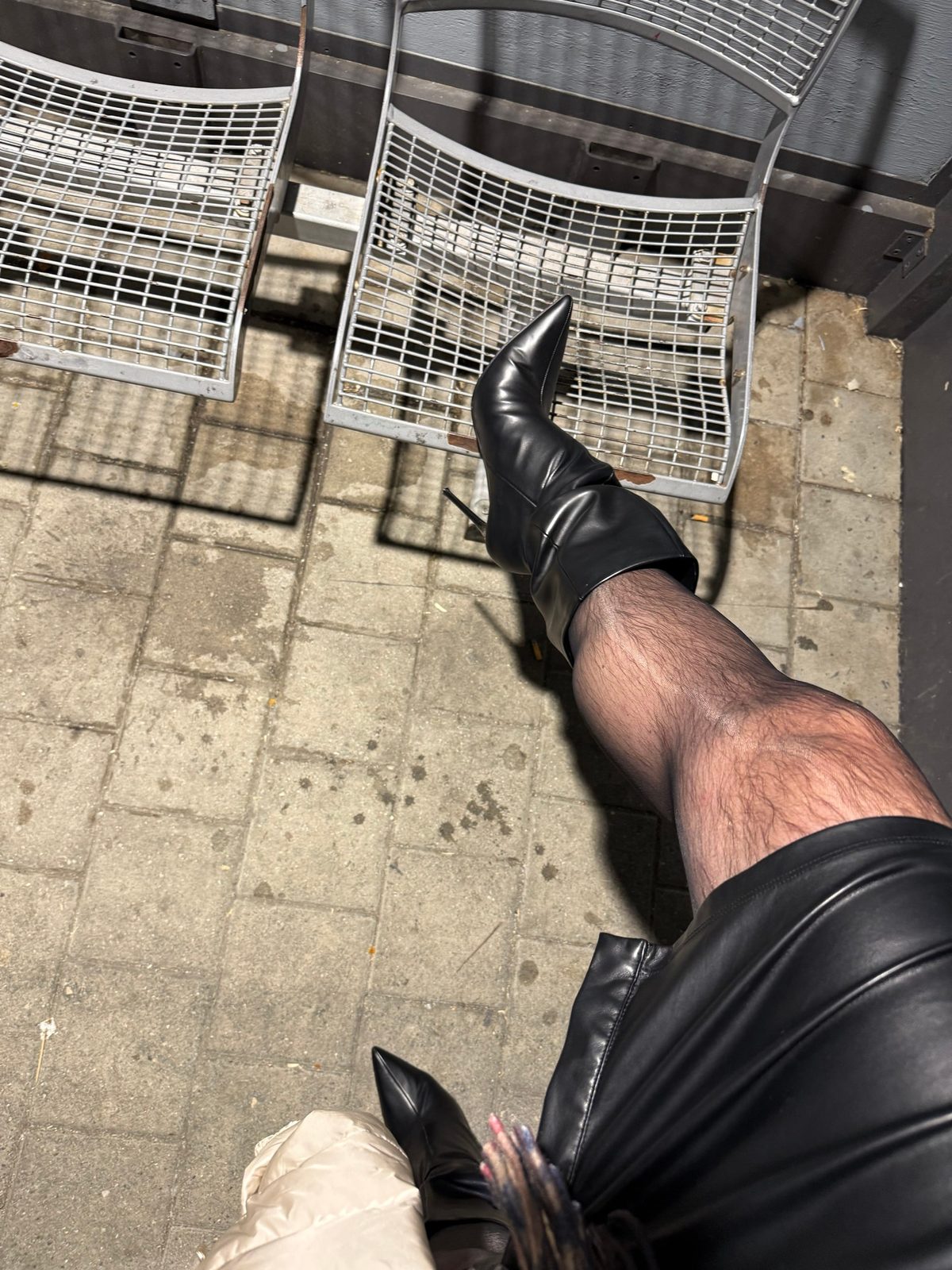 High black boots with a stiletto heel, leg raised in front of metal benches at the station