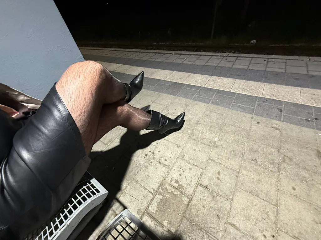 Legs in black tights and pointed black boots, crossed on a bench on a station platform at night